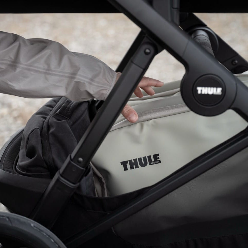 Person placing a Thule bag into the storage basket of a Thule stroller