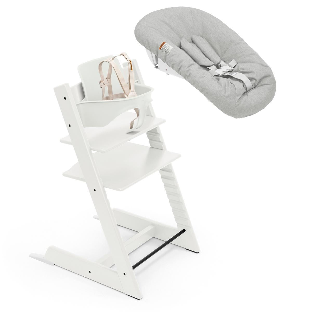 White wooden high chair with beige harness and grey newborn set by Stokke, shown in open box view with adjustable legs and safety straps.