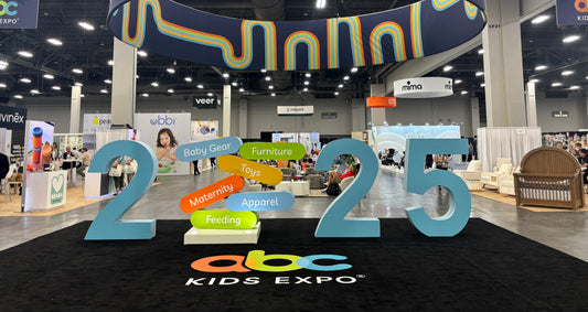 A vibrant and bustling ABC Kids Expo scene, featuring large "2025" display and product category signs, hinting at exciting new baby gear.
