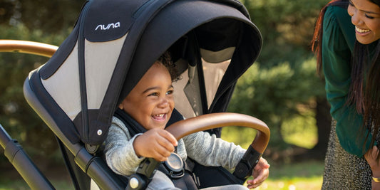 A cheerful toddler sits in a Nuna stroller, smiling at a woman, showcasing a top convertible stroller option.
