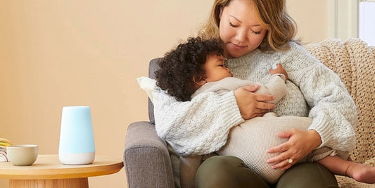 A loving mother holds her sleeping baby in a cozy nursery, next to a soothing sound machine, embodying peaceful rest.
