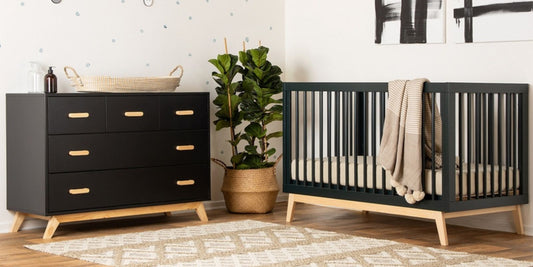 A modern nursery scene with a dark crib, dresser, leafy plant, and a cozy, neutral rug, exuding a calm, welcoming atmosphere.
