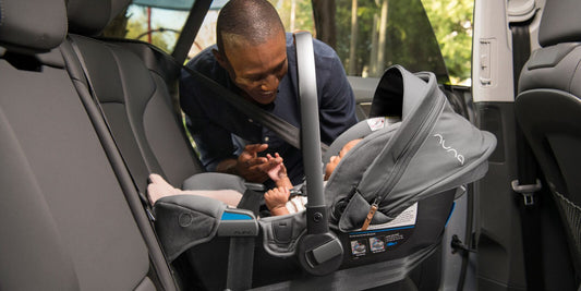 A smiling grandfather lovingly gazes at his grandchild secured in a Nuna car seat in the back of a car.
