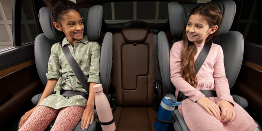 Two smiling girls are safely buckled in booster car seats, conveying security and peace of mind for parents.
