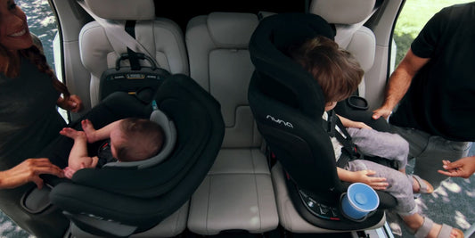 Two happy parents secure their children, a baby and toddler, into rotating car seats in a bright, modern vehicle. 
