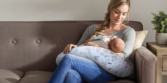 A serene moment: a mother lovingly breastfeeds her newborn on a comfy, floral-patterned nursing pillow on a sofa.
