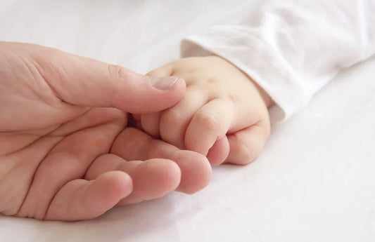 An adult hand gently holds a newborn's tiny hand, symbolizing the loving bond between parent and child.
