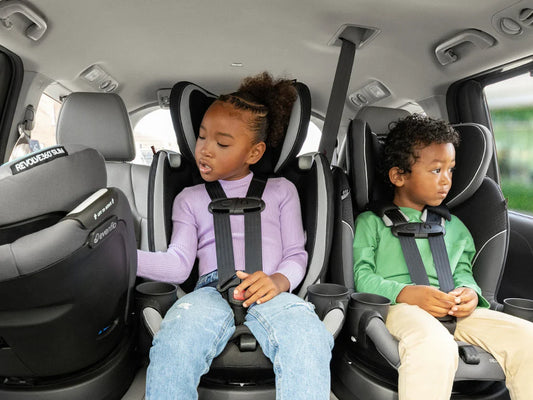Two young children sit safely buckled in car seats in the back of a vehicle, highlighting child passenger safety.