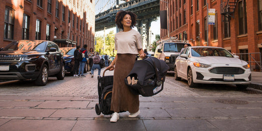 A stylish mother confidently walks in Brooklyn carrying a Nuna car seat, showcasing the brand's urban appeal.
