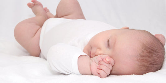 A baby sleeps peacefully on their back, fingers near their mouth, highlighting the safety of this sleep position.
