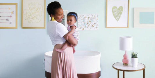 A smiling mother lovingly holds her baby near a smart bassinet, creating a warm and nurturing nursery scene.
