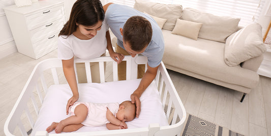 Parents lovingly gaze at their peacefully sleeping baby in a white crib, conveying warmth and the joy of a growing family.
