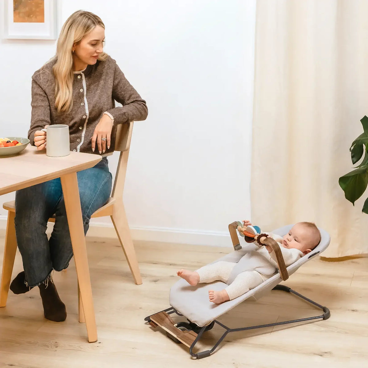A parent adjusts a baby in a gray UPPAbaby Mira Bouncer, conveying comfort and modern family lifestyle.
