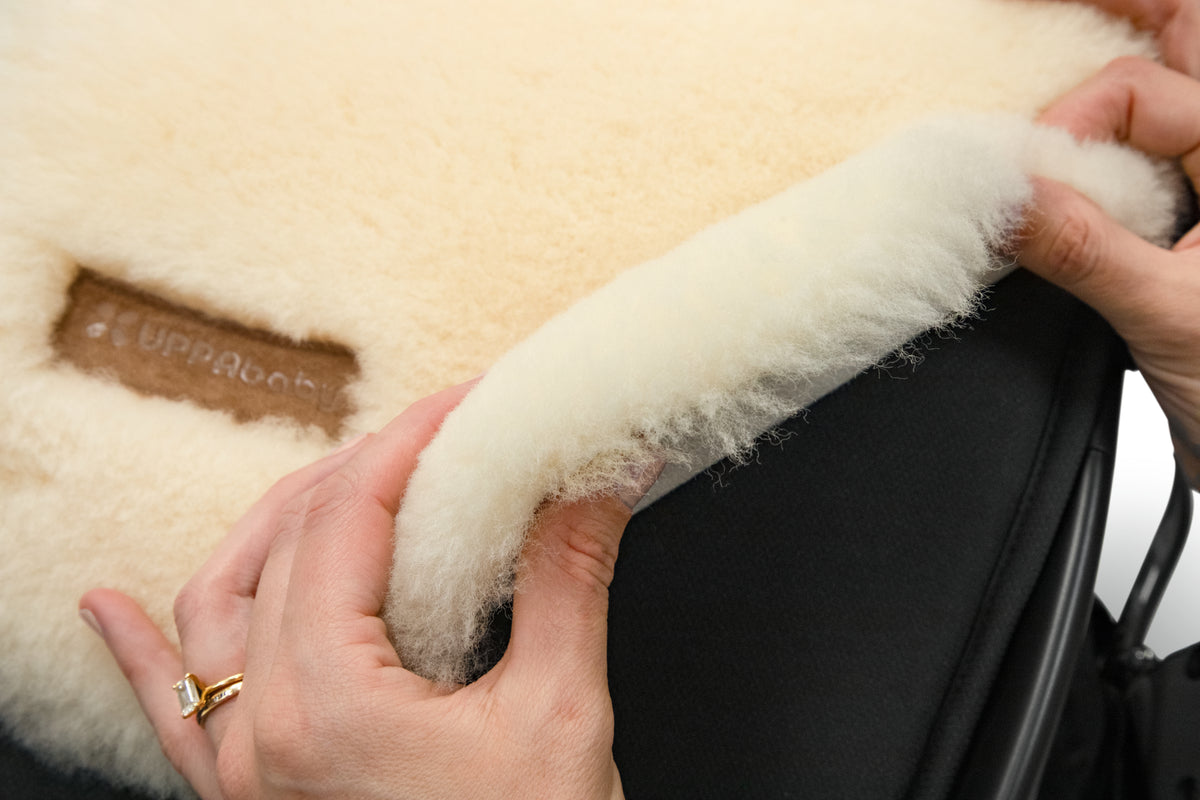 Hands holding a cream colored UPPAbaby sheepskin stroller liner
