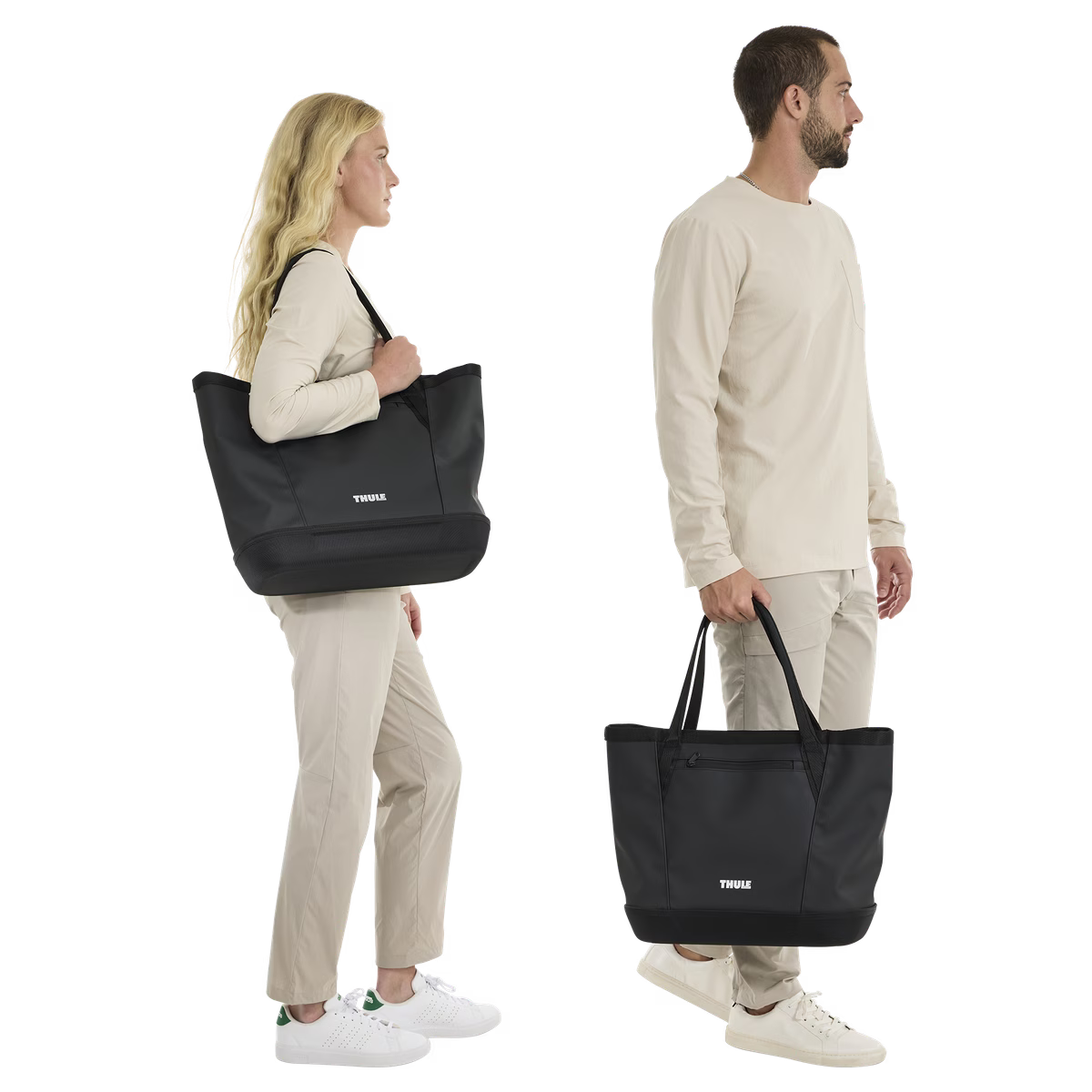 Black Thule Chasm Gear Tote 30L by Thule, shown in lifestyle side view with models carrying, featuring durable fabric, front logo, and dual handles.