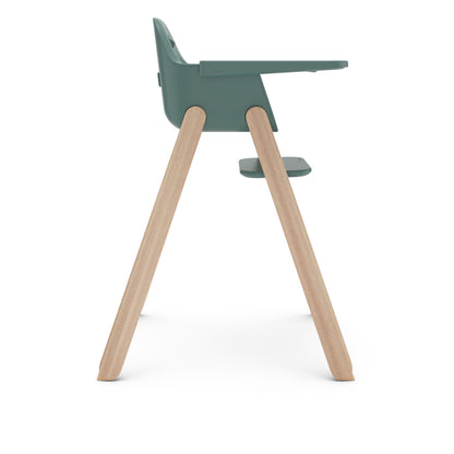 Side view of a green plastic high chair with light wood legs and a footrest