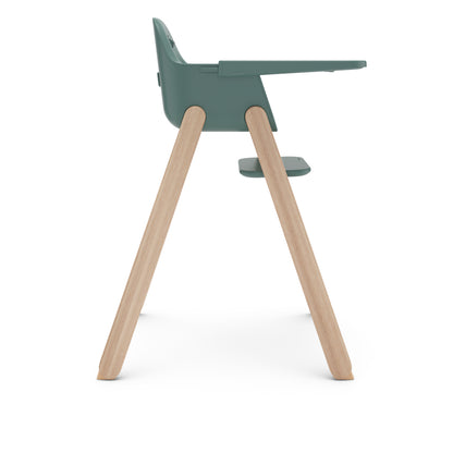 Side view of a green high chair with light wood legs and a tray