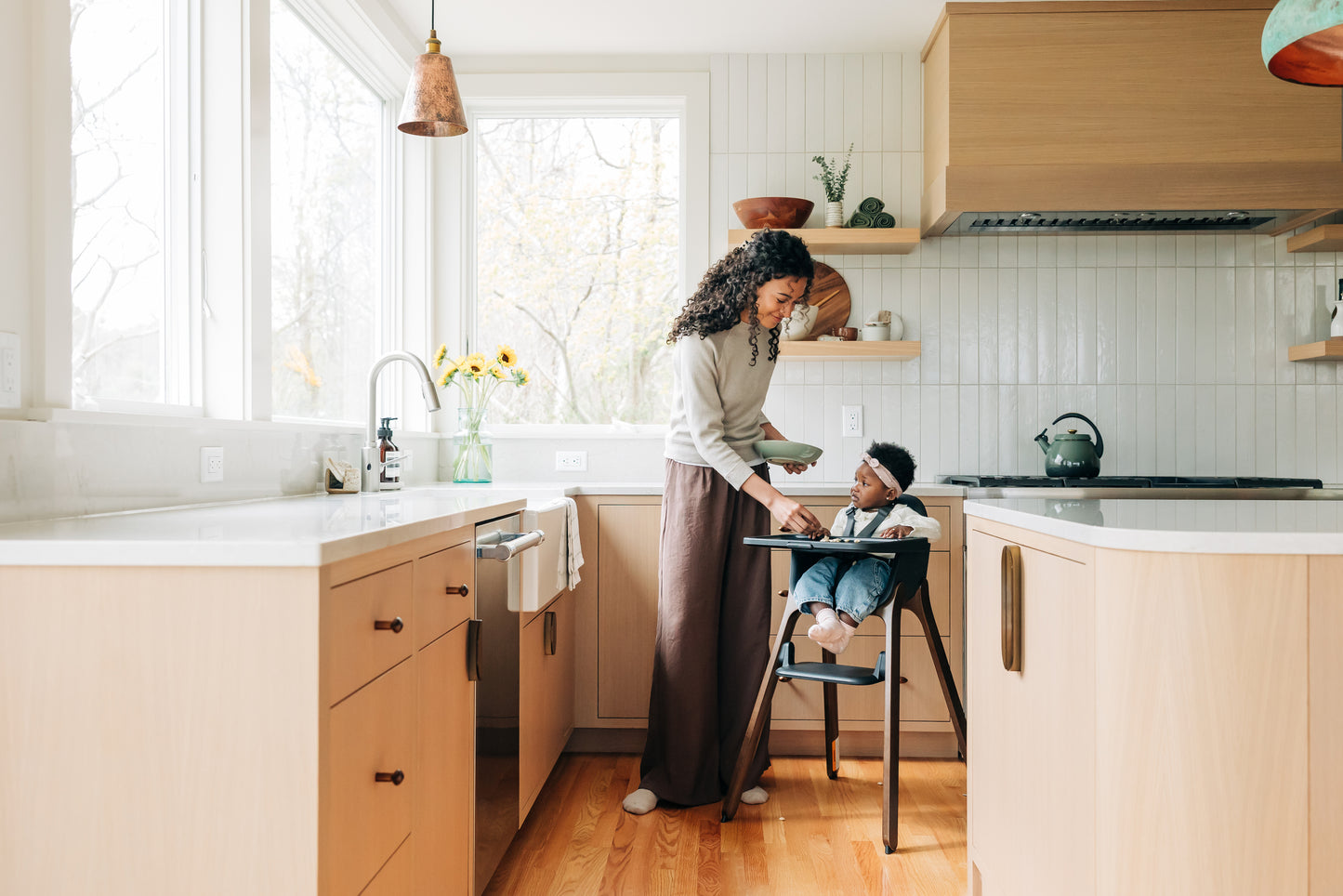 Woman feeding a baby in a high chair in a modern kitchen