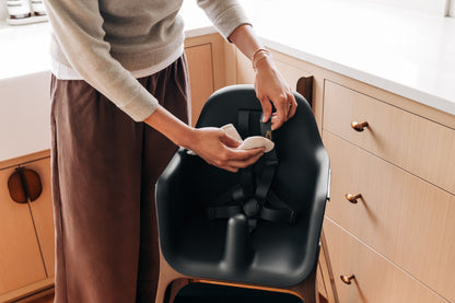 Person cleaning the harness of a black high chair with a cloth