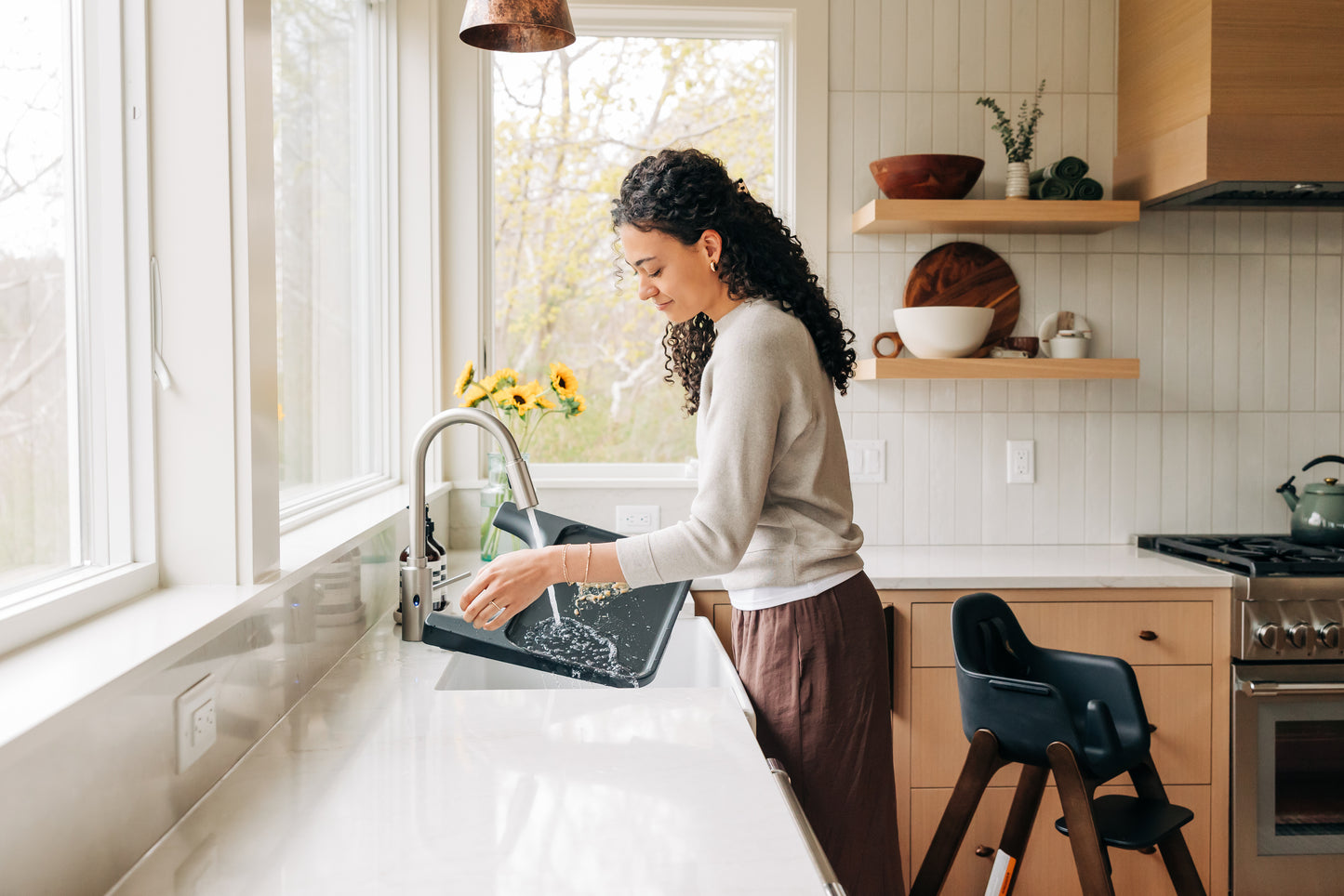 Woman rinsing a black high chair tray under a kitchen faucet