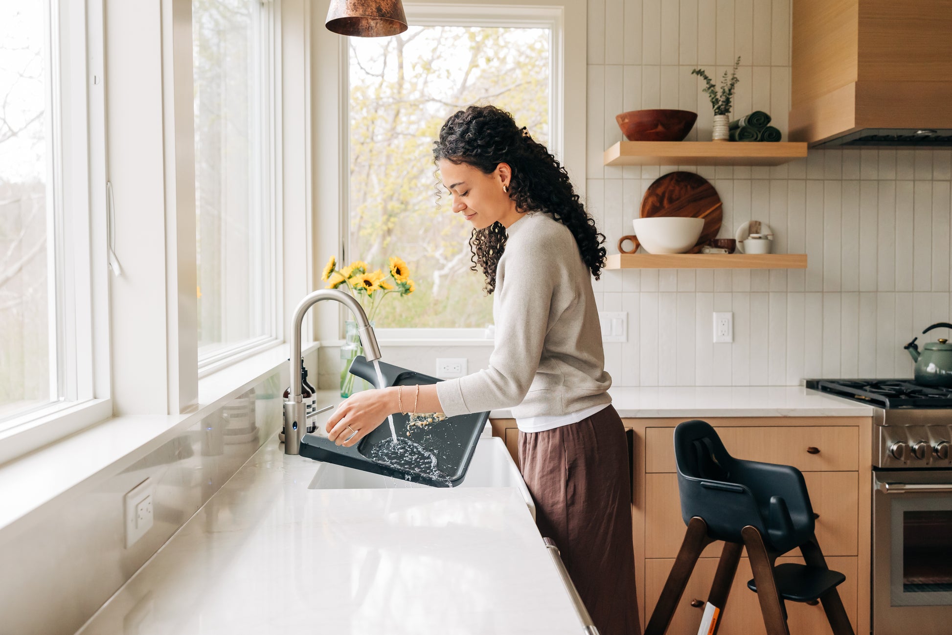 Woman rinsing a black high chair tray under a kitchen faucet