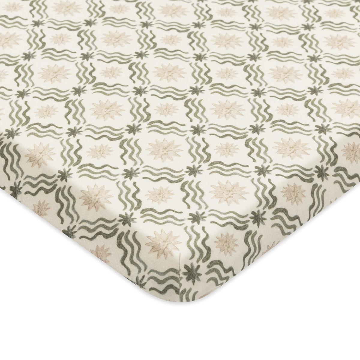 Babyletto crib sheet with a cream background featuring a repeating pattern of green wavy lines and beige starbursts