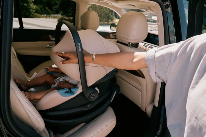 Interior of a car with a baby in a Cybex car seat, installed on a light beige leather seat, a hand adjusting it.