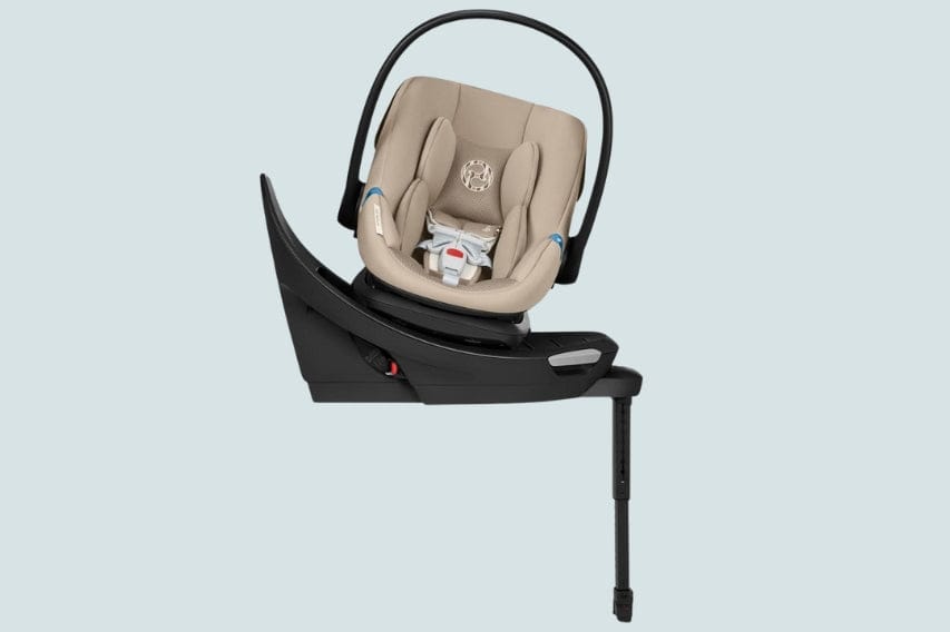 A beige infant car seat sits on a black base with a support leg extended downwards on a pale blue background.