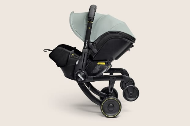 Modern black stroller with mint green canopy, four wheels, and attached storage bag, viewed from side on neutral background.