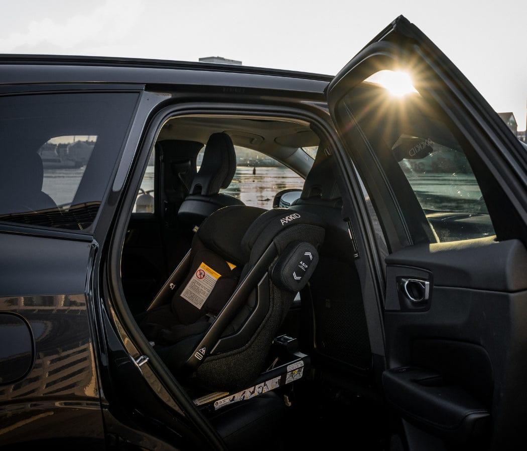 Black car interior with open door, child safety seat installed, sun shining through window, waterfront background.