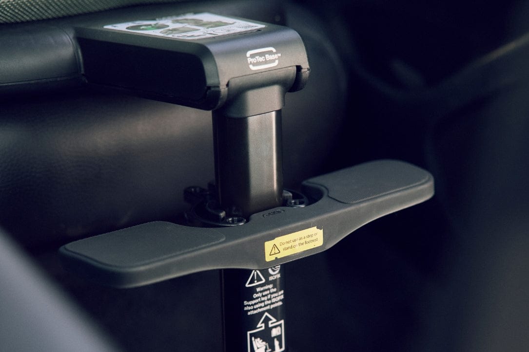 Close-up of black ProTec Base™ car seat support with yellow warning label, mounted in vehicle.