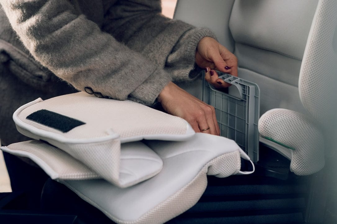 Hands attach white car seat cover to gray plastic frame inside vehicle, soft fabric and mesh texture visible.