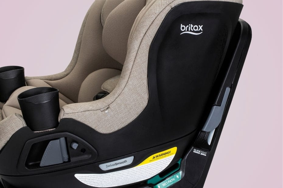 Close-up of a Britax car seat. It has black cup holders, "SwivelSmooth", "WARNING!", "BELT PATH" and "CLICKTIGHT" labels, and beige padding. The background is pink.