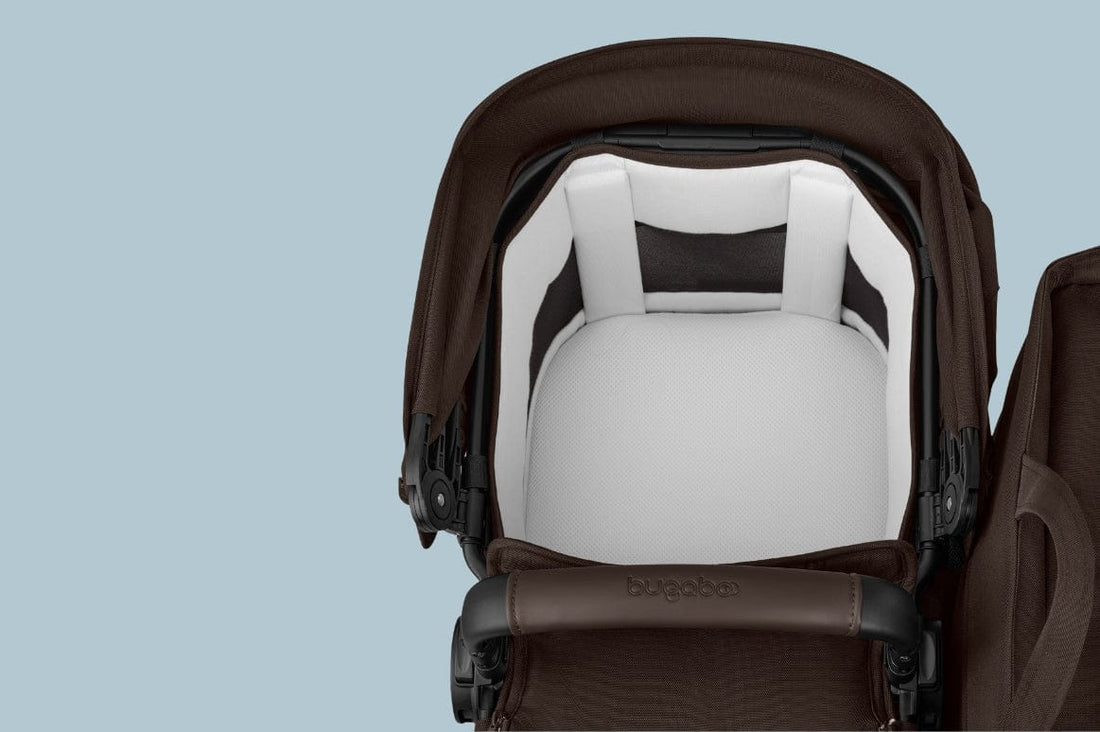 Brown and white Bugaboo stroller seat with padded interior, black frame, and brand logo on handlebar, against light blue background.