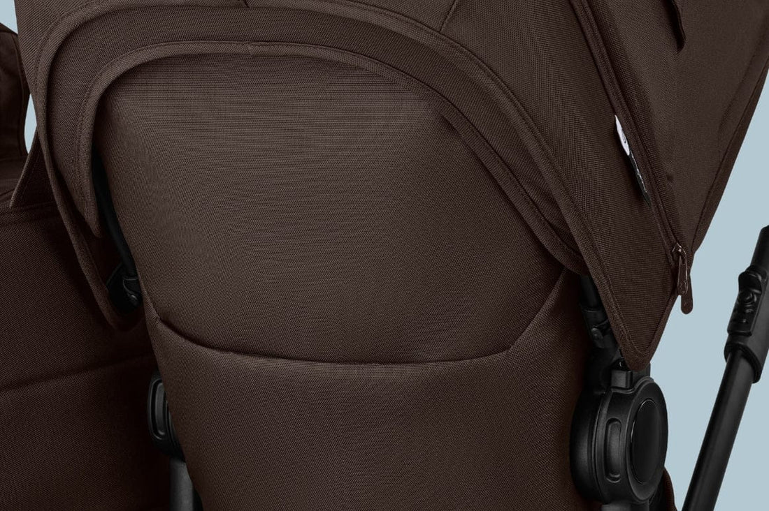 Close-up of brown stroller seat with textured fabric, black plastic joints, and zipper detail on side.