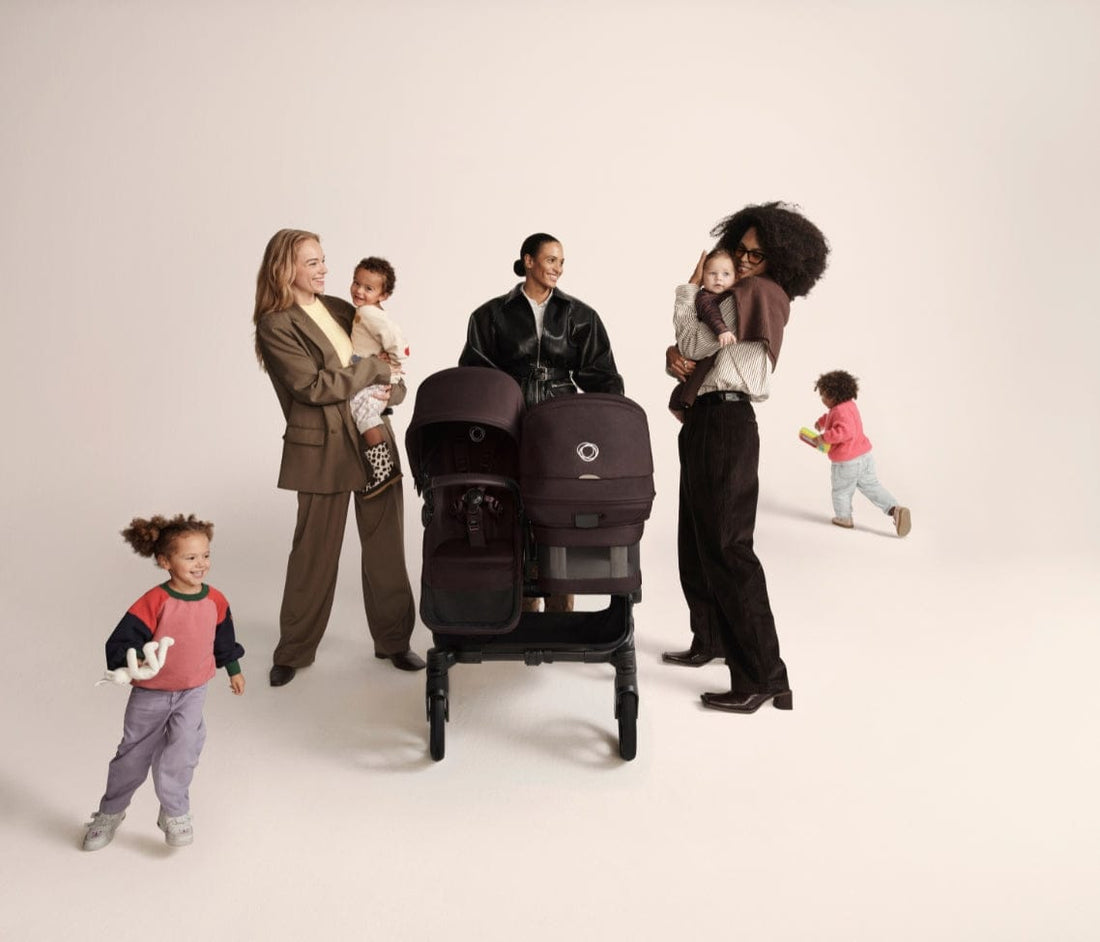 Three women with children pose around a dark brown double stroller against a neutral background, showcasing modern family life.