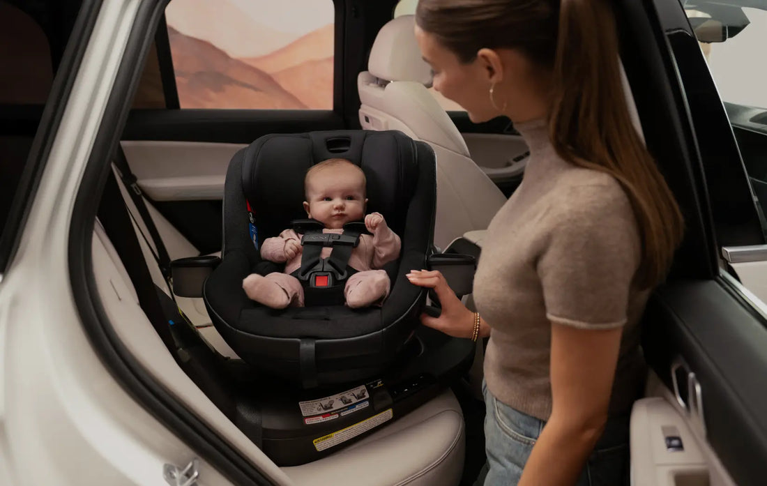 Nuna revv maxx 360 convertible car seat with baby and mother inside of a white vehicle.