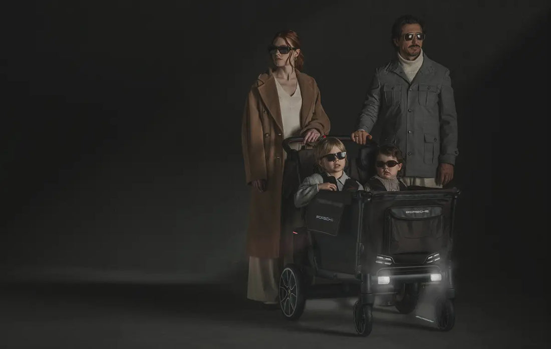 man and woman standing together with porsche wonderfold wagon with two children in the seats everyone is wearing sunglasses.