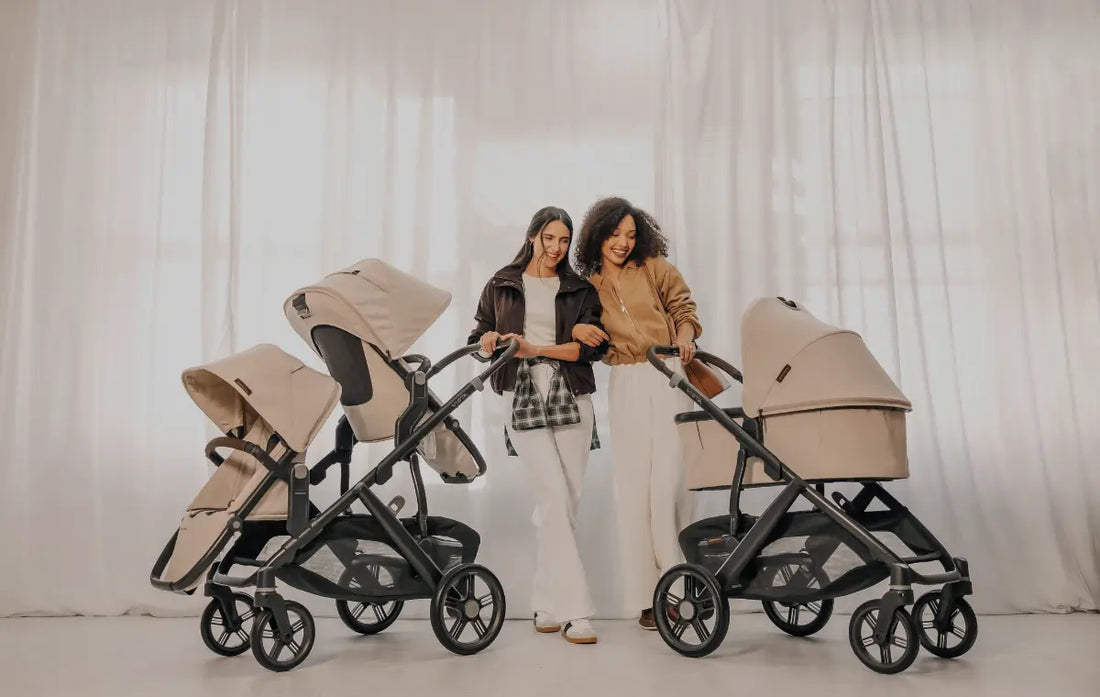 Two women standing in a beige room with one stroller as a double with two seats and one with a bassinet in the new Ada color from UPPAbaby - now at Albee!
