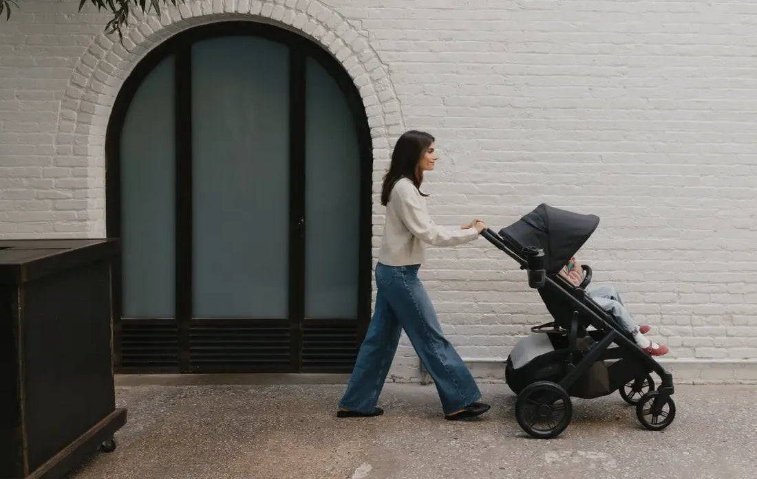 mom pushing child in the uppababy vista v3 in jake charcoal against a brick building.