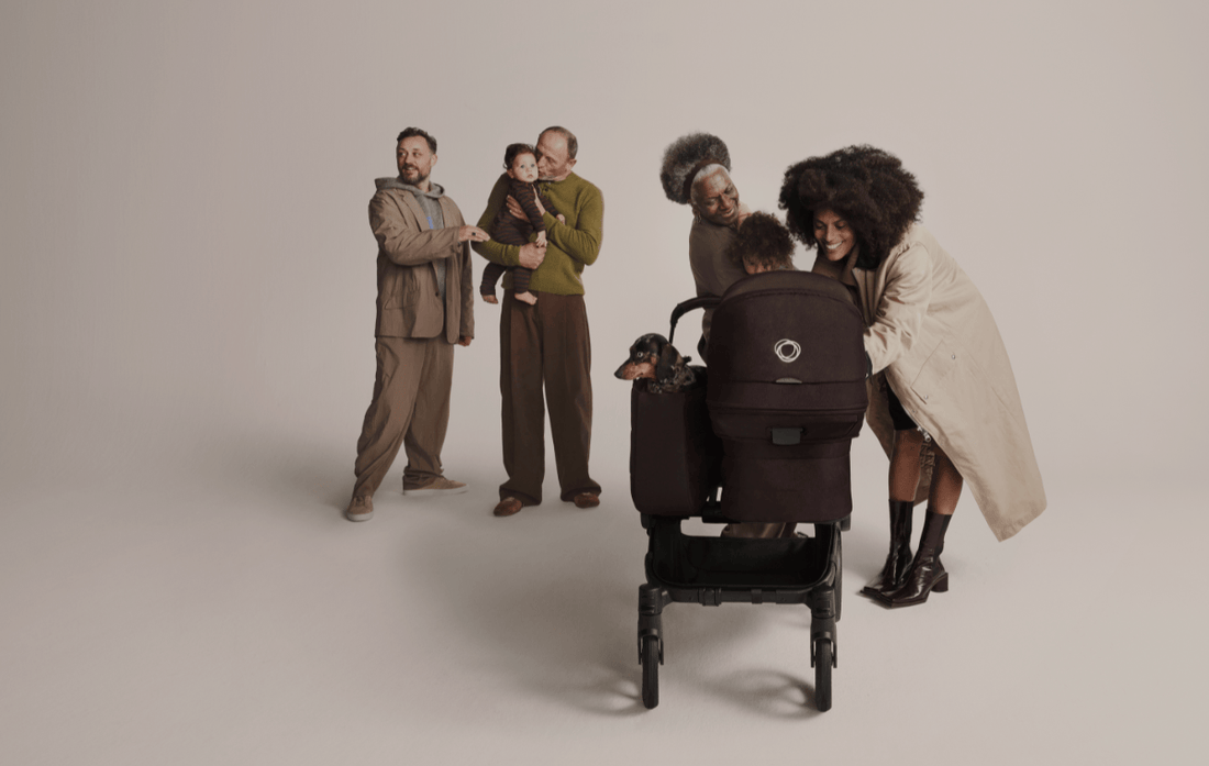 family gathered around bugaboo donkey 6. 2 mothers holding infants with two twin toddlers running around and childless woman in the middle pushing stroller - new at albee baby.