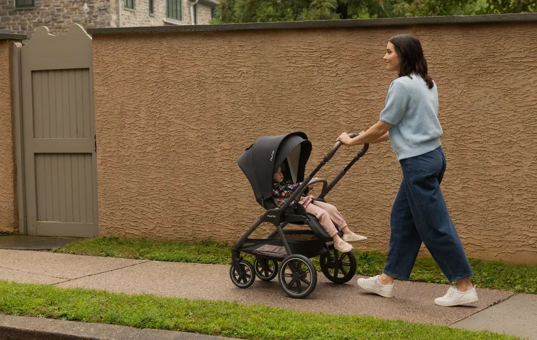 nuna triv lx stroller with toddler girl sitting in the seat being pushed by a mother down the sidewalk.