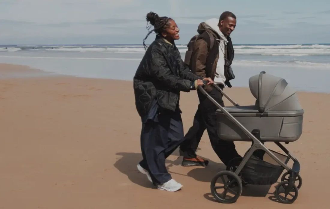 man and woman pushing silver cross cove 2 stroller with bassinet on a beach.