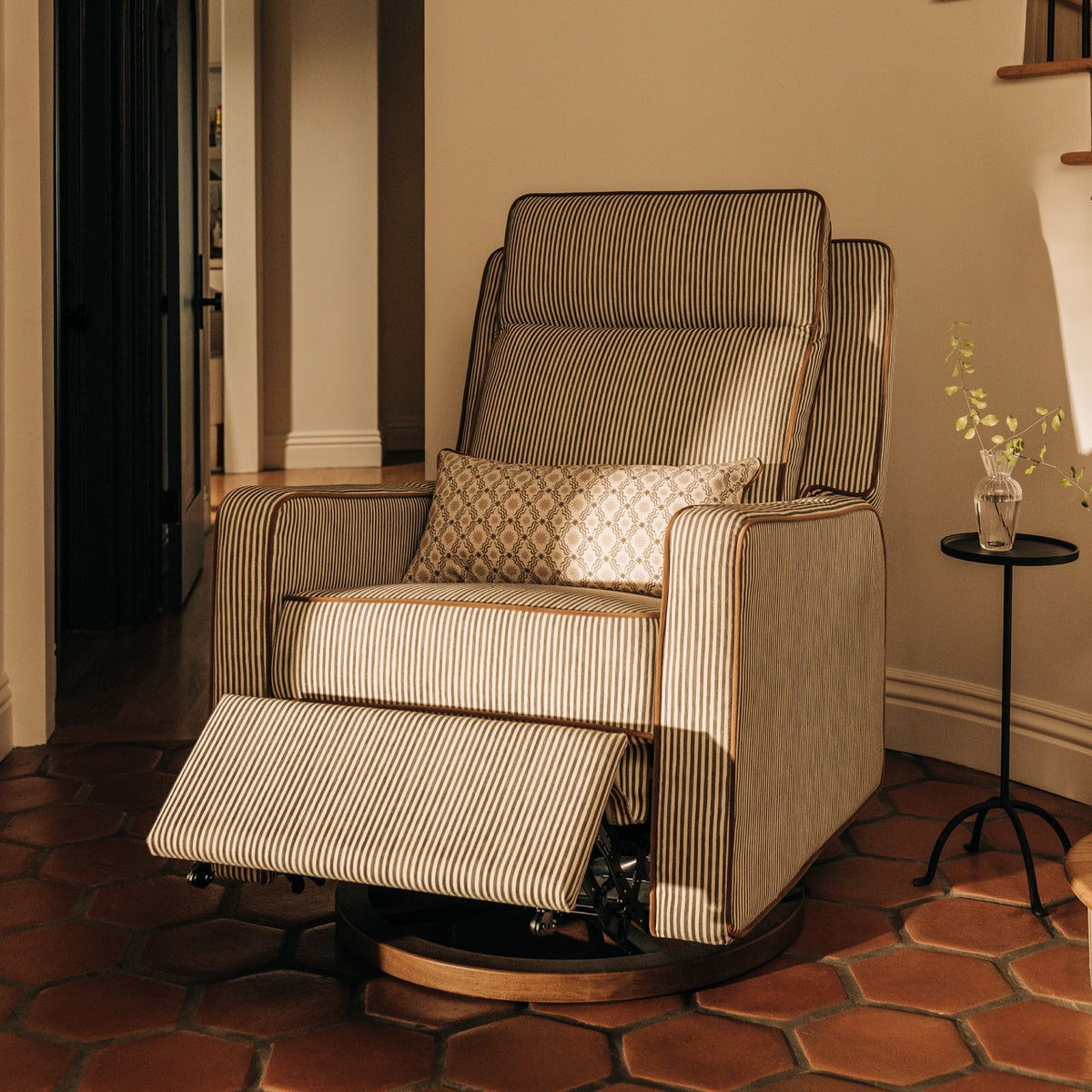 Babyletto striped recliner with a patterned lumbar pillow on a terracotta tile floor
