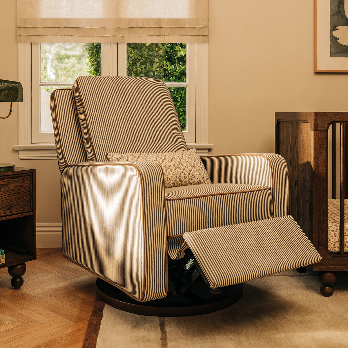 Babyletto striped swivel glider recliner with footrest extended in a nursery