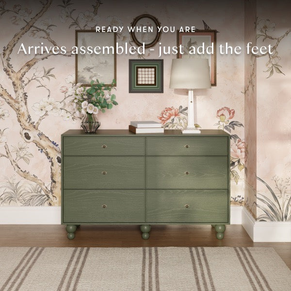 Babyletto six drawer dresser in olive green with round feet against floral wallpaper