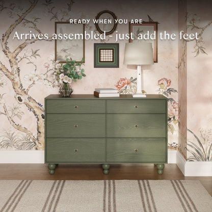 Babyletto six drawer dresser in olive green with round feet against floral wallpaper