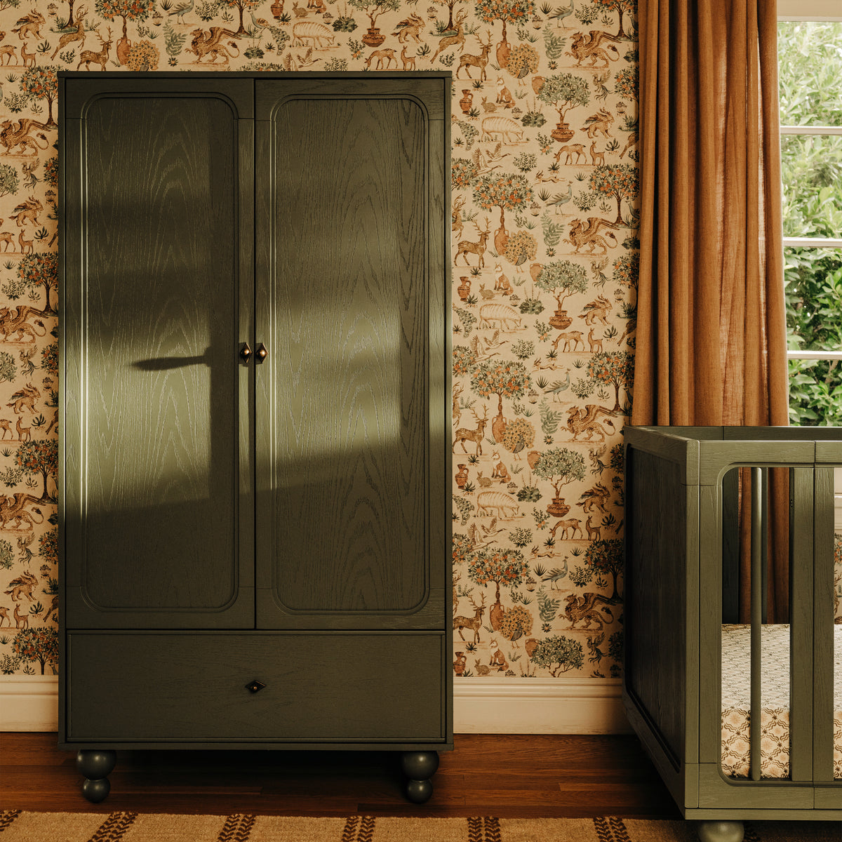 Babyletto olive green wooden wardrobe with two doors and a bottom drawer against patterned wallpaper