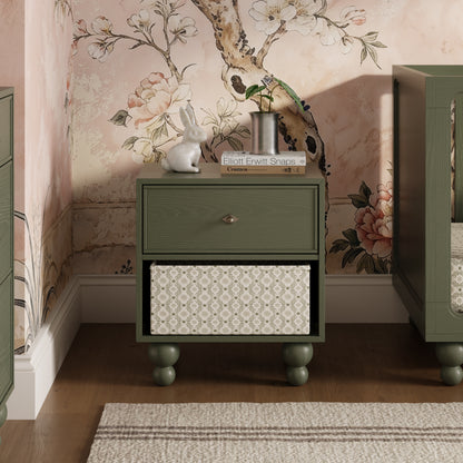 Babyletto olive green nightstand with one drawer and open storage shelf containing a patterned bin