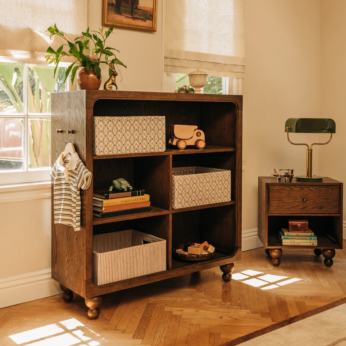Babyletto dark wood bookshelf with storage bins and toys next to a matching nightstand